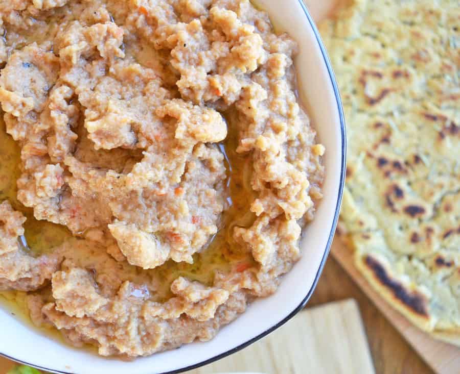 A textured aubergine peanut butter dip in a white bowl beside a flatbread