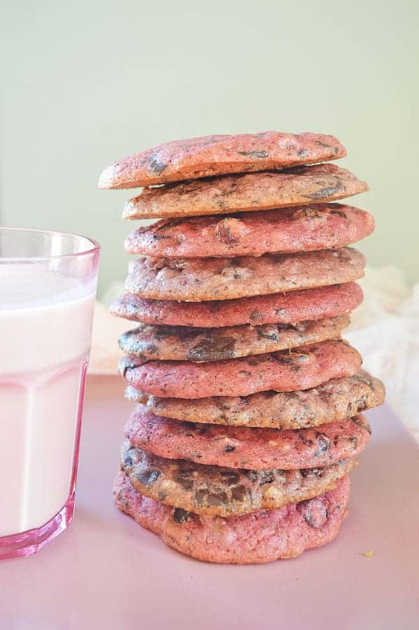 A stack of pink and purple cookies next to a glass with non-dairy milk in it