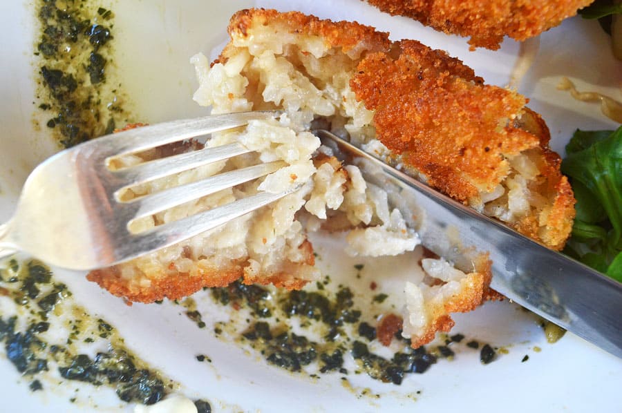A fork and knife cutting into a rice croquette on a white plate