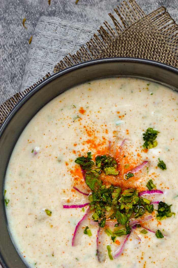 A closeup of a bowl of raita with red onion and fresh cilantro on top