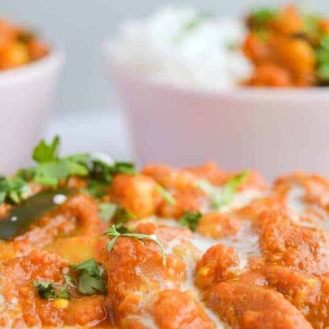A closeup of orange curry sauce with chickpeas, an dtwo bowls of it with rice in the background