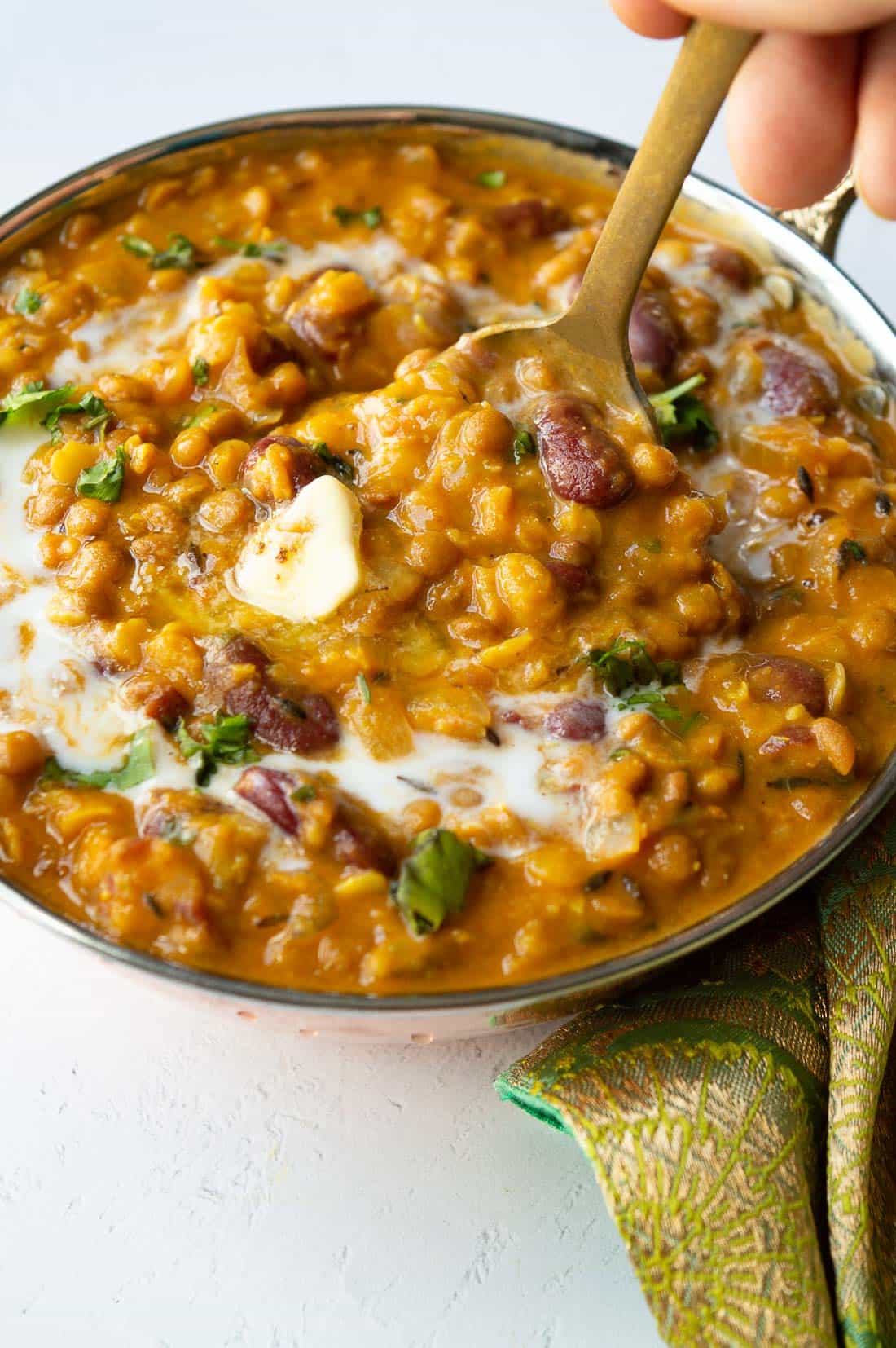 A copper bowl with lentil and kidney bean curry being stirred.