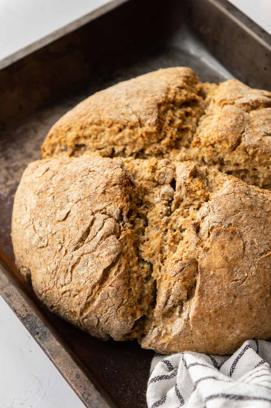 Soda bread with a cross cut in it in a metal tray.