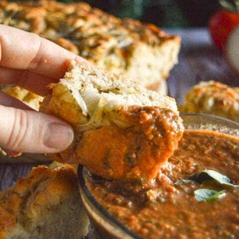 A hand dipping a slice of focaccia into a tomato herb dip