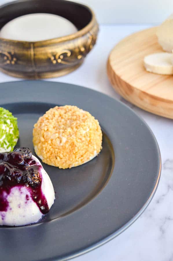 A dark grey plate with three cheeses rolled in toppings