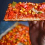 A thin pizza slice loaded with thick sauce and vegetables
