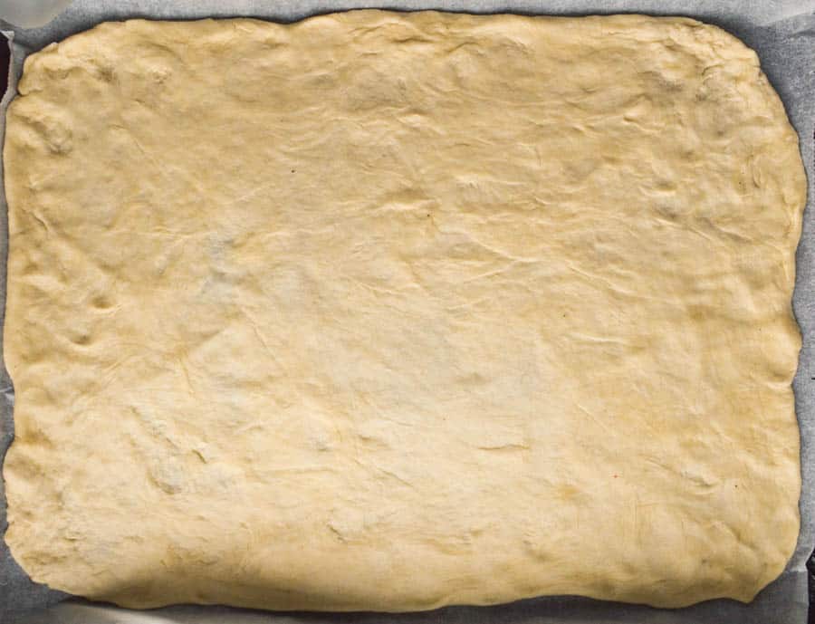 Thinly rolled out pizza dough on a large rectangular baking tray