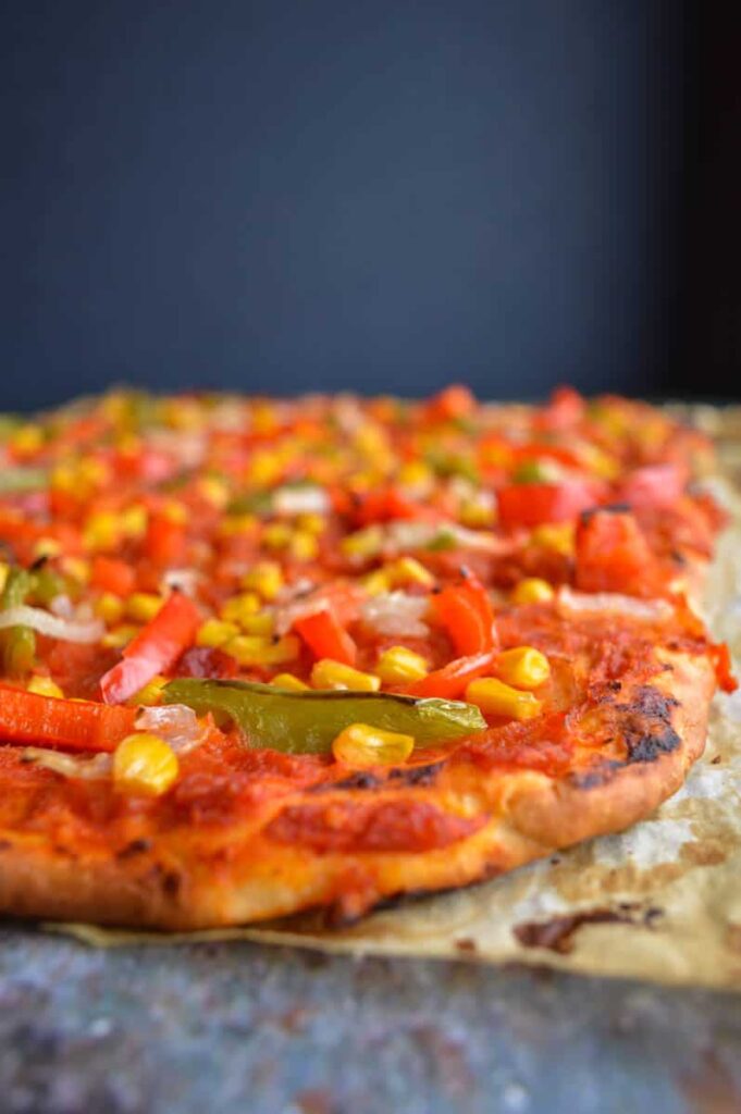 A tomato and vegetable pizza viewed head on with a dark blue and grey background