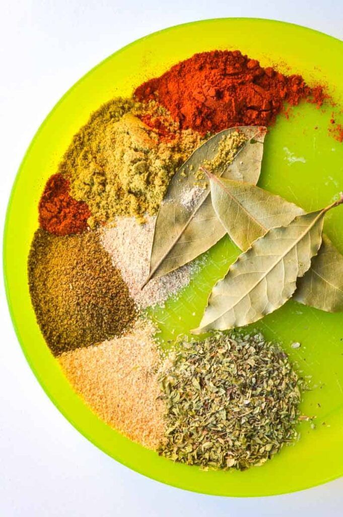 Several colourful spices and bay leaves on a green plate