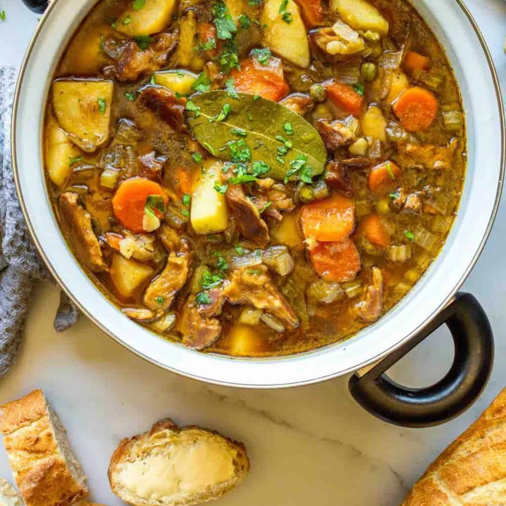 Top down view of a pot with vegetables in a brown liquid with a sliced baguette below it