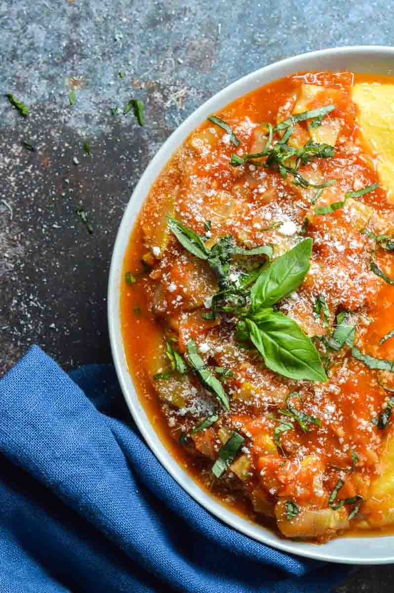 A white bowl with marinara dish of zucchini and fresh basil on top