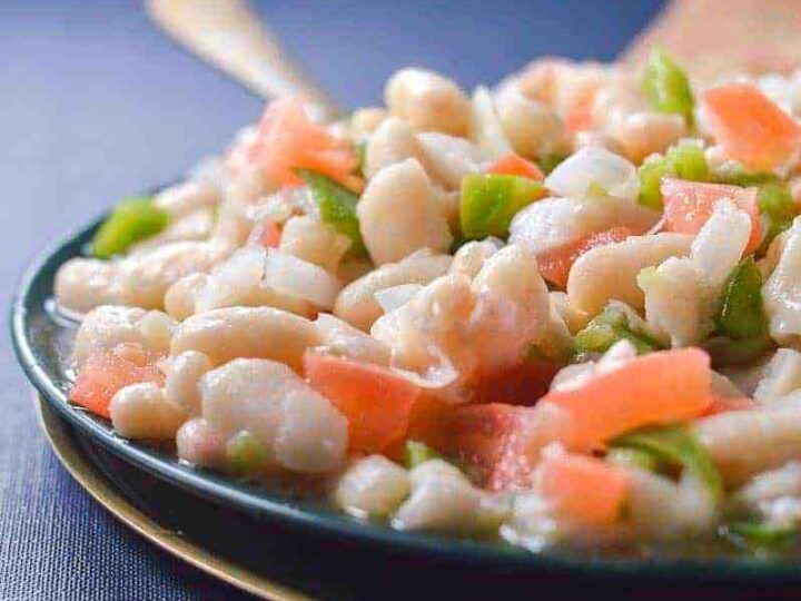 Close up of a white bean salad on a blue dish on a blue tablecloth