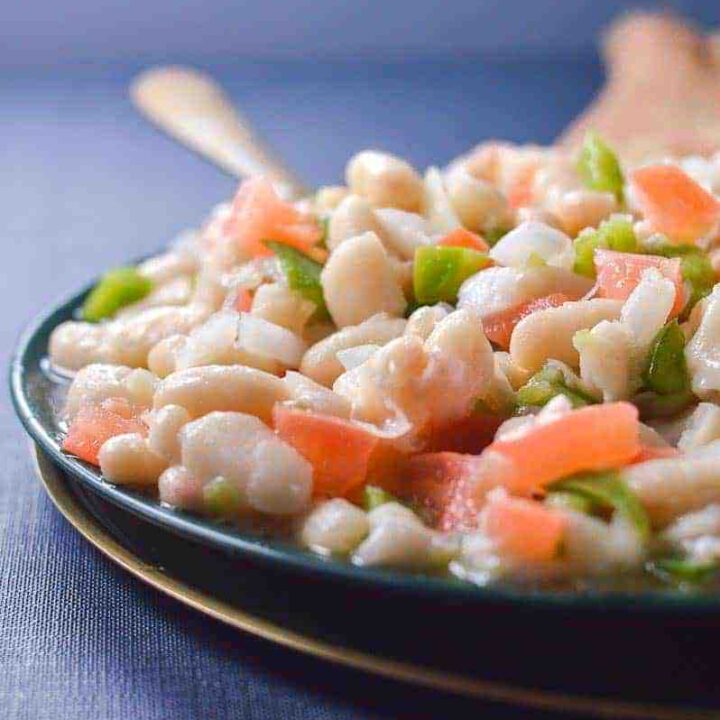 Close up of a white bean salad on a blue dish on a blue tablecloth