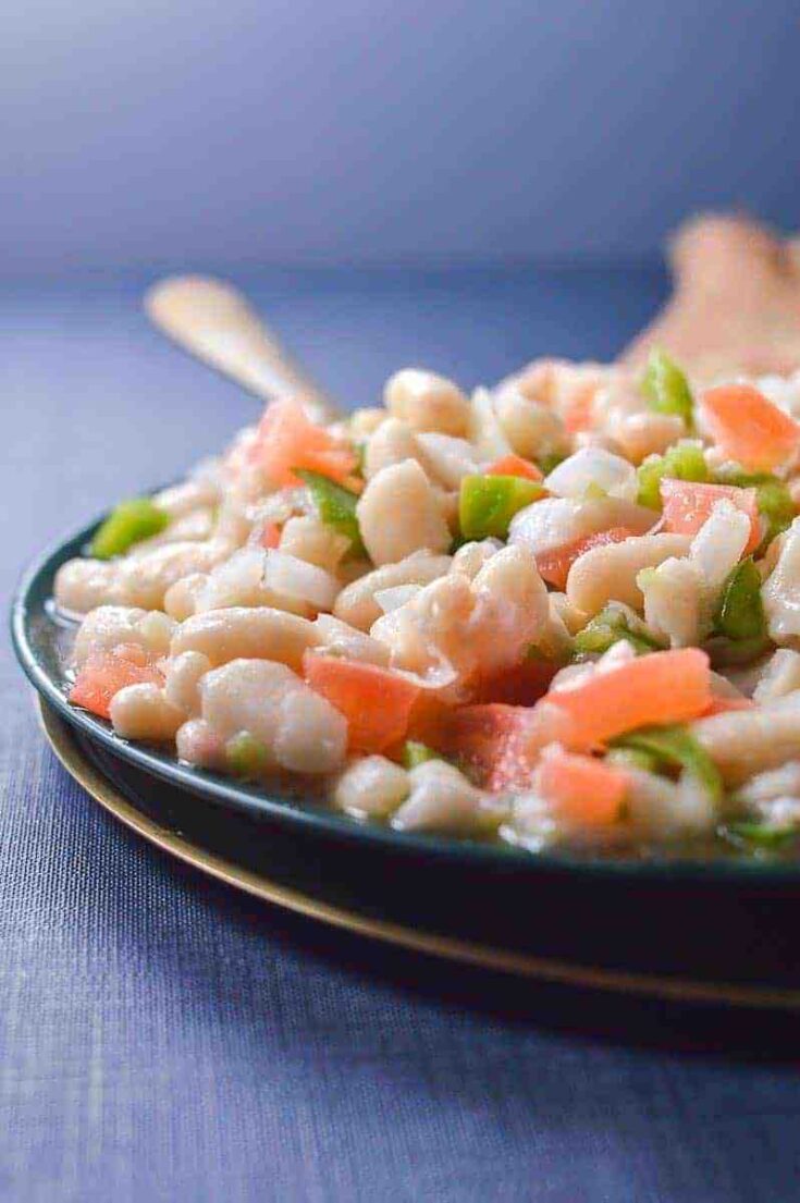 Close up of a white bean salad on a blue dish on a blue tablecloth