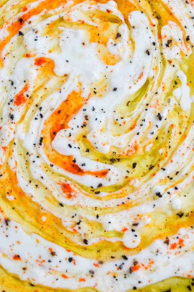 A close/up of white creamy dip with olive oil and paprika swirled through