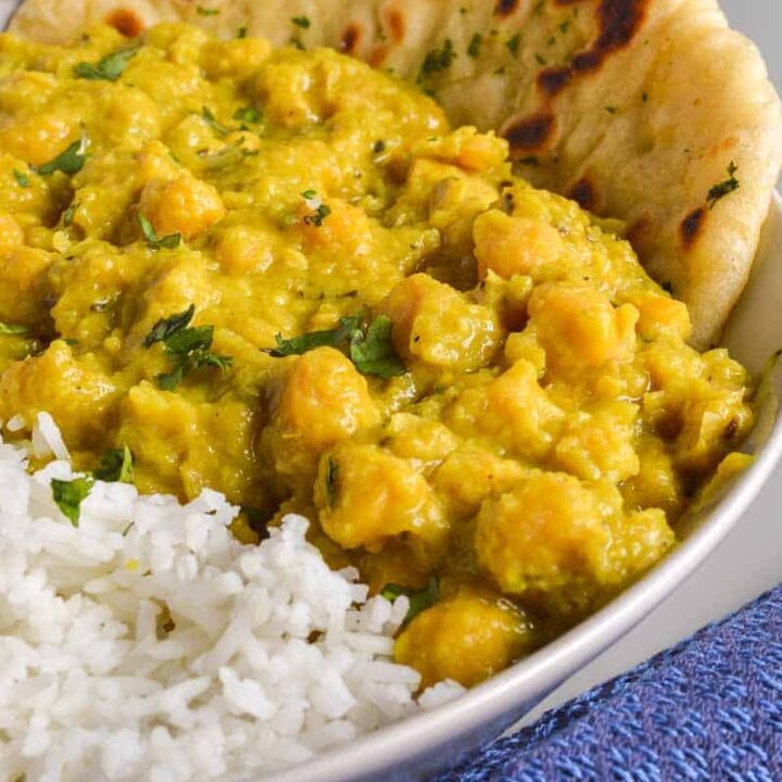 A yellow creamy chickpea curry in a bowl with naan bread