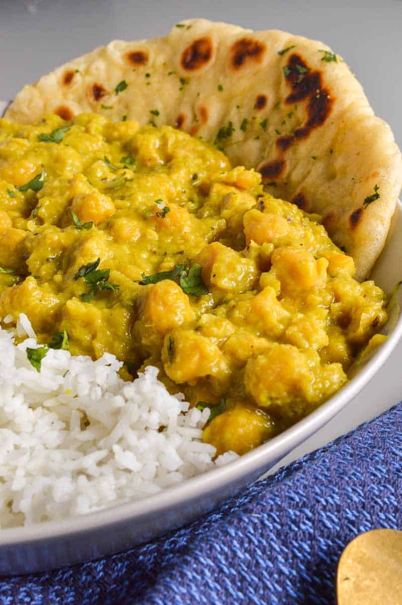 A yellow creamy chickpea curry in a bowl with naan bread