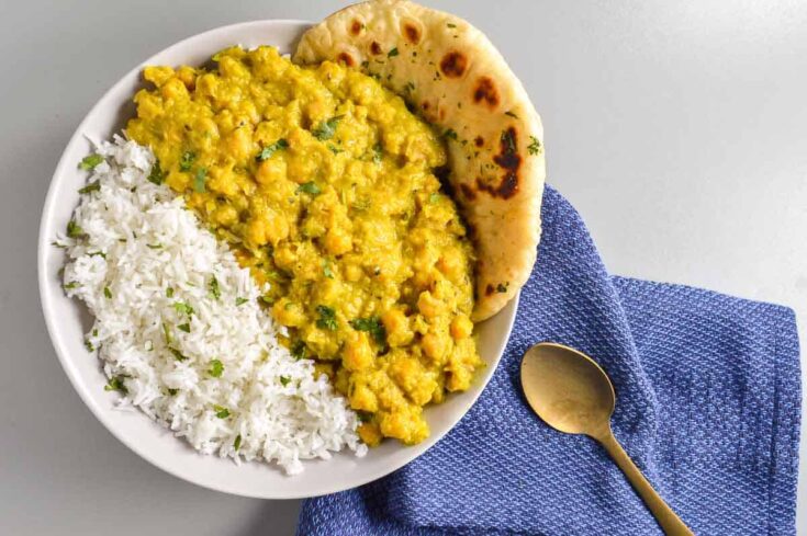 A bowl of golden chickpea curry and rice on a dark blue cloth