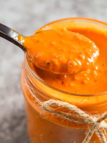 Closeup of a black spoon with slightly chunky orange sauce