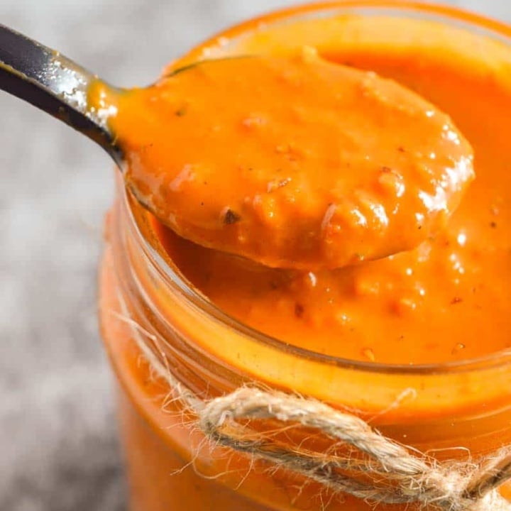 Closeup of a black spoon with slightly chunky orange sauce