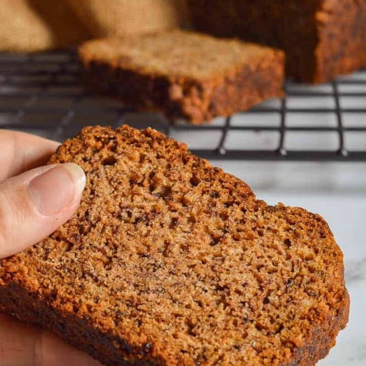 A dark slice of quick-bread with a loaf in the background