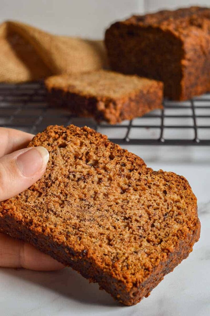 A dark slice of quick-bread with a loaf in the background