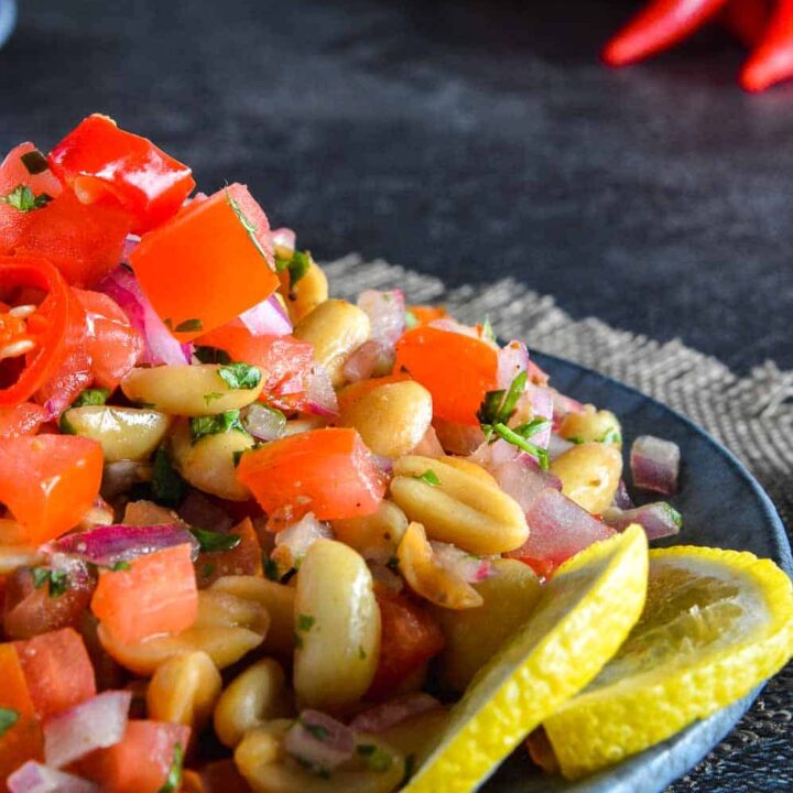 Close up of peanuts, coriander, lemon slices and tomatoes with red chili peppers in the background