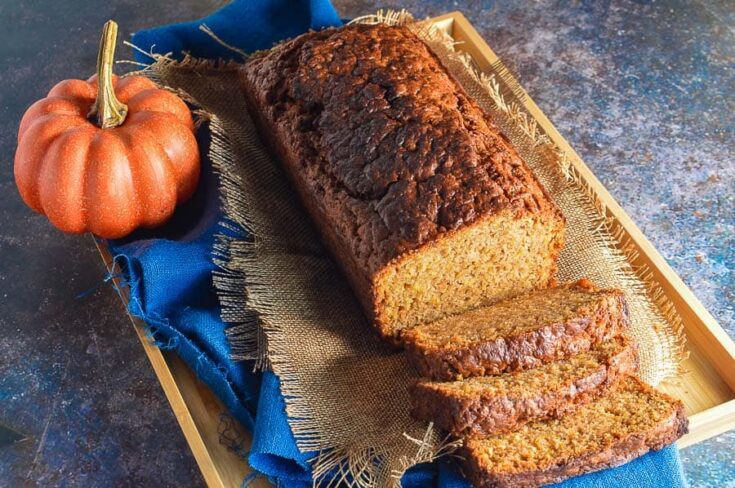 A gold brown loaf with several slices and an orange pumpkin