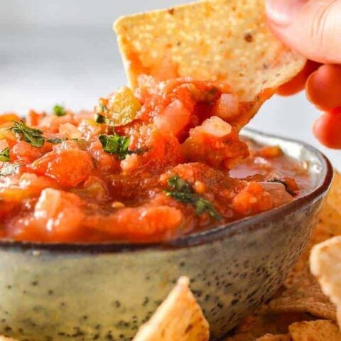 A tortilla chip being dipped into a bowl of chunky salsa
