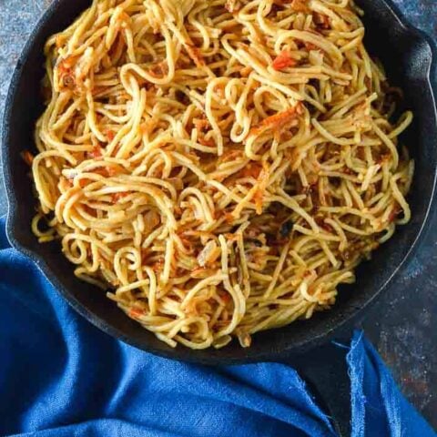 A top down look at spaghetti fried in a cast iron pan on a blue background