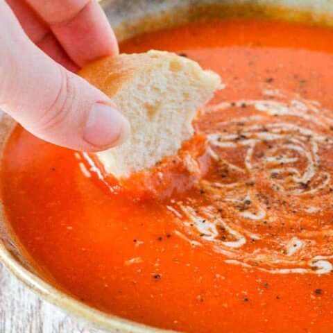 A woman's hand dipping bread into a bowl of tomato soup