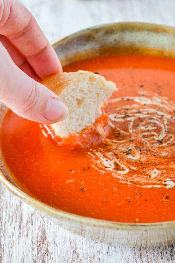 A woman's hand dipping bread into a bowl of tomato soup
