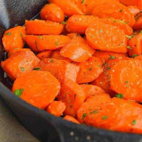 cast iron pan with glazed carrots sprinkled with parsley