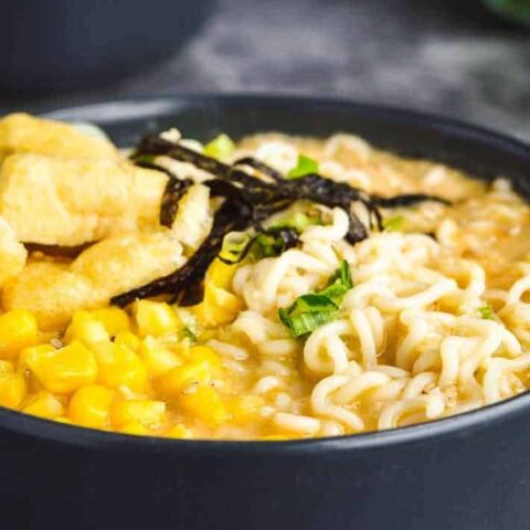 Side view of two gray bowls full of creamy broth, ramen noodles, spring onions, tofu and sweetcorn