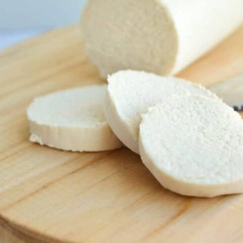 Cover image of vegan goat cheese web story with a log of cheese and three slices on a wooden board