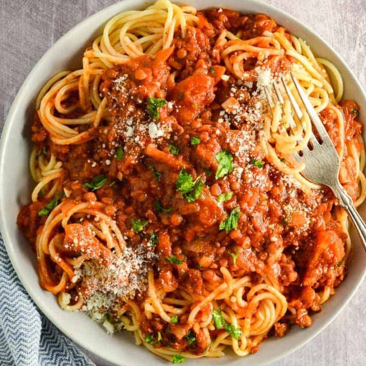 Overhead view of a bowl of lentil bolognese and spaghetti on a grey background