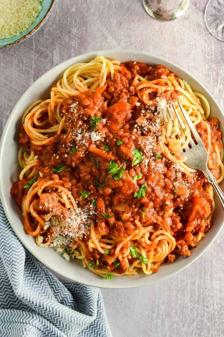 Overhead view of a bowl of lentil bolognese and spaghetti on a grey background
