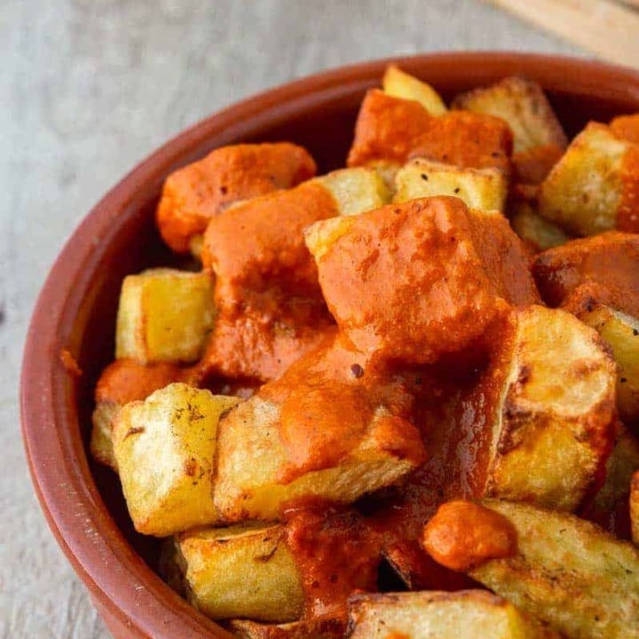 fried potatoes in a terracotta dish covered with red-brown bravas sauce