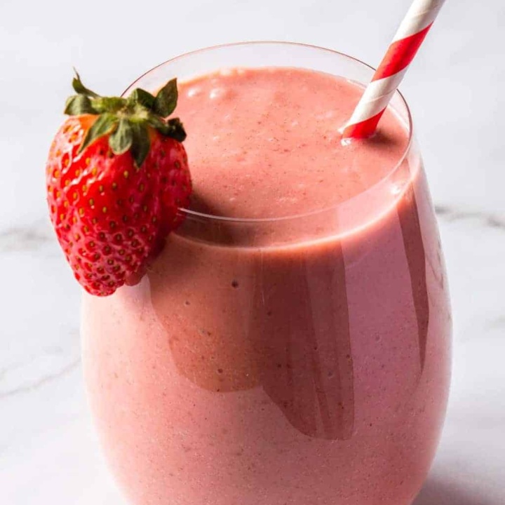 Front view of a round glass with a pink smoothie, a strawberry on the rim, and a red and white paper straw