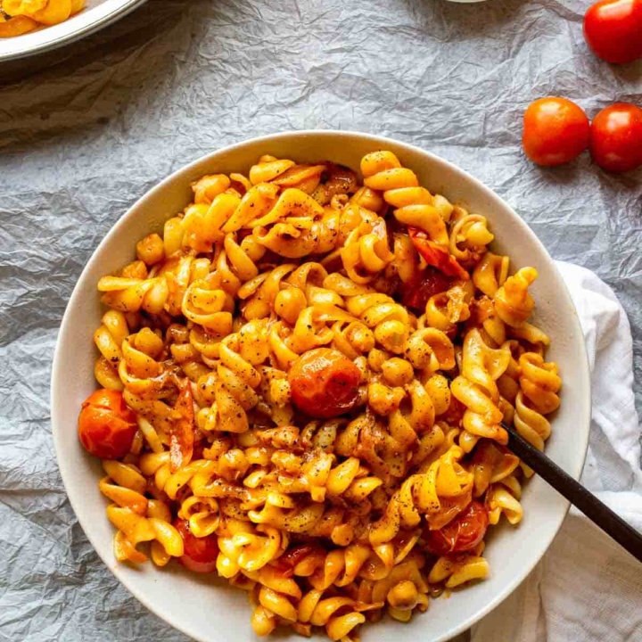 Top down view of a bowl of pasta with cherry tomatoes and an orange sauce, on a pale grey background