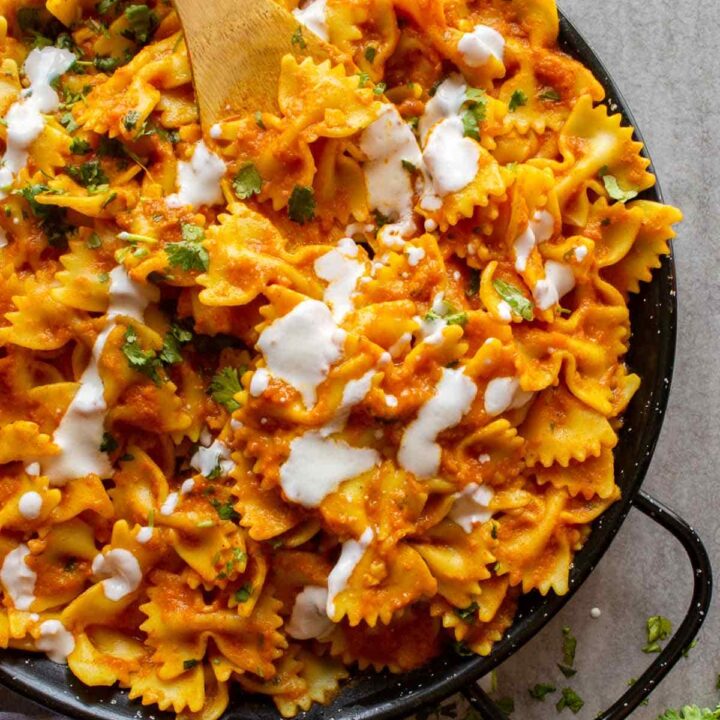 A black cast iron pan with pasta coated in orange sauce with white cream drizzled over