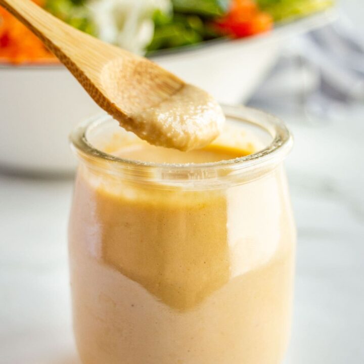 A wooden spoon dipping into a small glass jar of creamy light brown dressing.