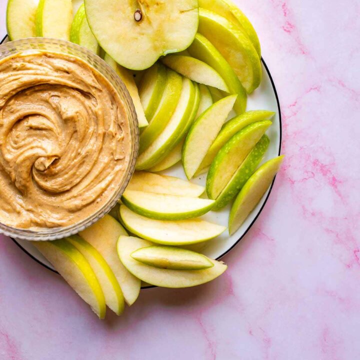 Pink background with a plate of green sliced apples and brown dip on it.