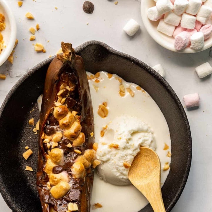 Black cast iron pan with a baked banana and melting ice-cream with a wooden spoon in it.