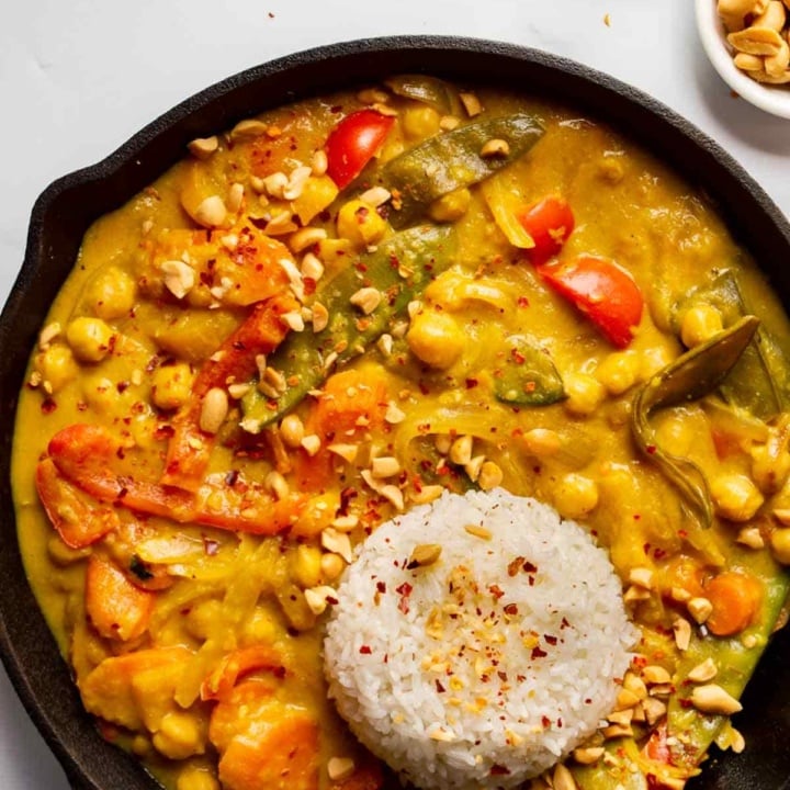 Overhead view of cast iron pan with a yellow curry with chickpeas and vegetables and a round pat of white rice.