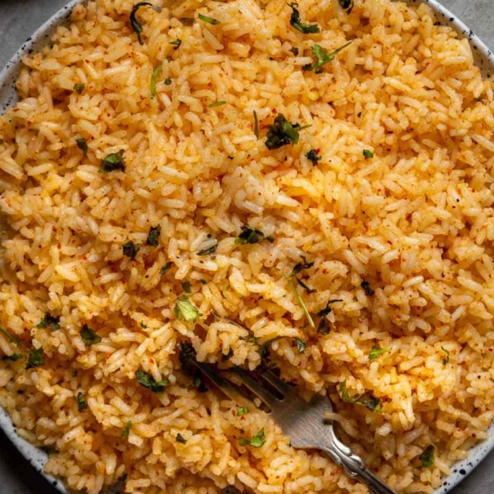 Top-down shot of a large plate of orange rice on a grey background.