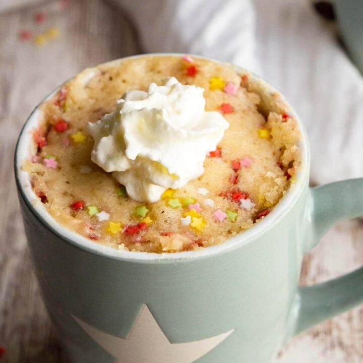 Green mug with a white star and a funfetti cake with cream on top in it.