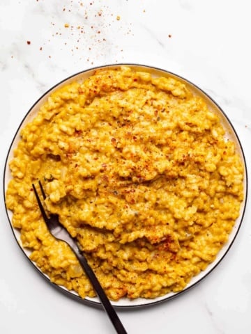 A plate of creamy orange rice on a white background with a black fork on it.