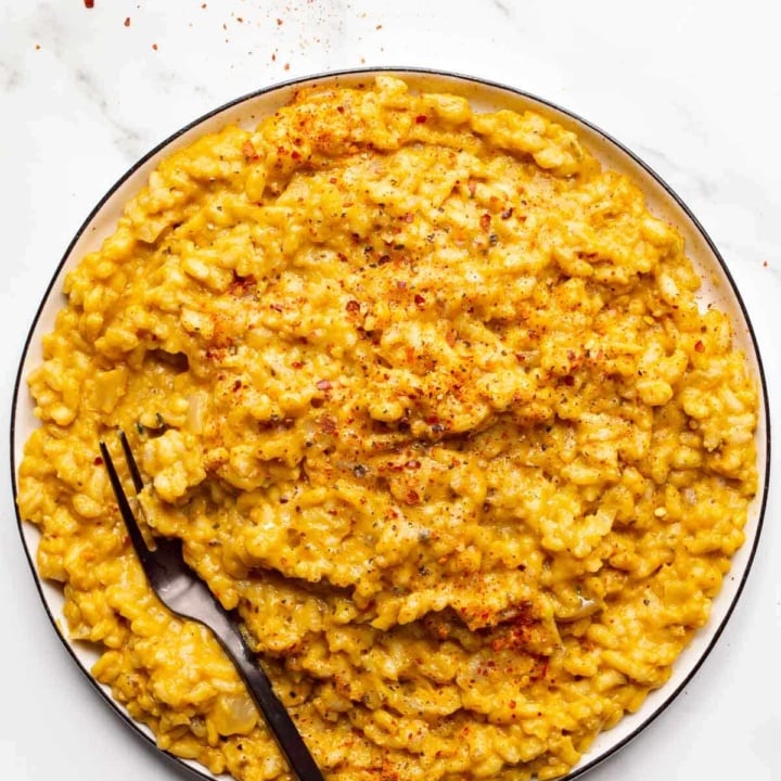 A plate of creamy orange rice on a white background with a black fork on it.
