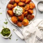 A plate of harissa roasted potatoes with a herbed white creamy dip on top.